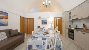 A dining area with a table set for four, a sofa, a kitchen with white cabinets, and a painting on the wall. - WePuglia - Donna Lisa (Polignano a Mare)