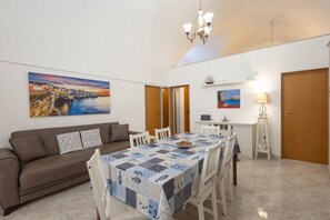 A dining area with a table set for four, a sofa, a laptop on a desk, and a painting on the wall.