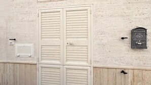 A white door with horizontal louvered panels, a mailbox, and a small electrical box on a textured wall. - WePuglia - Donna Lisa (Polignano a Mare)