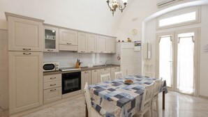 A kitchen with white cabinets, a microwave, a sink, and a dining table with chairs. - WePuglia - Donna Lisa (Polignano a Mare)