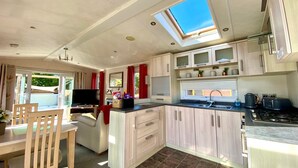 A compact RV kitchen with a skylight, a dining area with a table and chairs, and a TV.