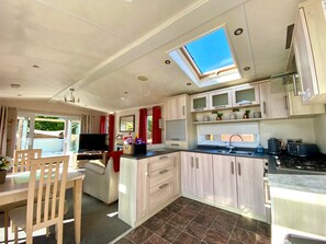 A compact RV kitchen with a skylight, a dining area with a table and chairs, and a TV.