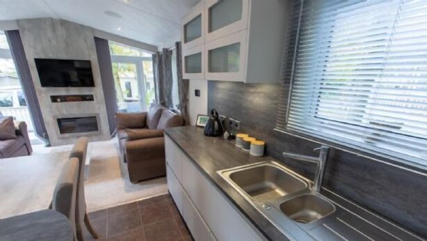 Una cocina moderna con horno empotrado, un lavamanos de acero inoxidable y una zona de comedor con sofá y mesa.