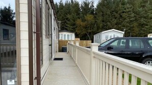 Una terraza de madera con barandilla blanca que lleva a un edificio con ventanas amplias y una puerta.