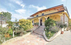 Stroll up the stone steps to the entrance of this charming two-story building, surrounded by lush greenery and vibrant flowers.