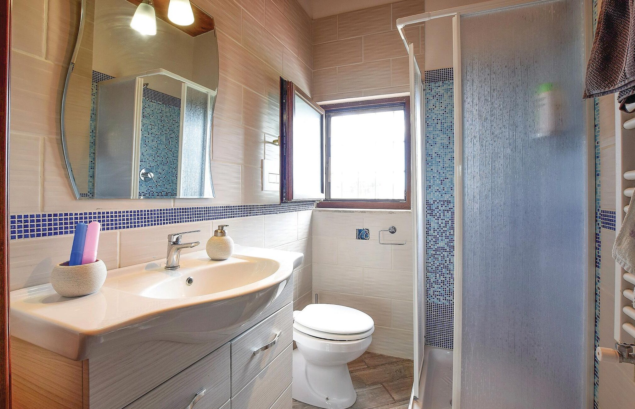 A bathroom with a sink, mirror, toilet, and shower area.