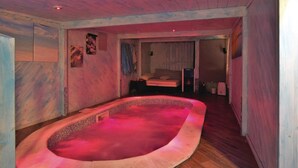 Ein Zimmer mit einer kleinen, ovalen Badewanne in der Mitte, einem Bett mit Kissen und einem an der Wand befestigten Regal mit verschiedenen Gegenständen.