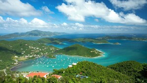 A coastal landscape with lush green hills, a bay with clear turquoise waters, and several small buildings. - The Honeymoon Suite with Private Hot Tub (St. John)