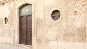 A weathered building facade with a large wooden door and two circular windows.