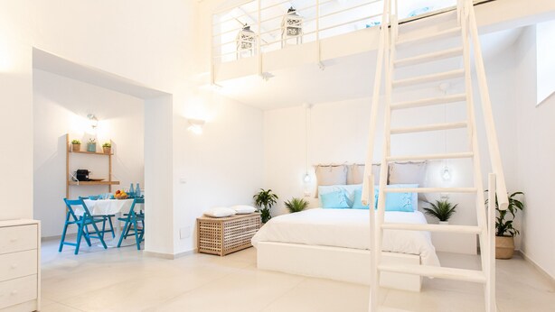 A modern, well-lit bedroom with a bunk bed, a dining area with blue chairs, and a kitchen area.