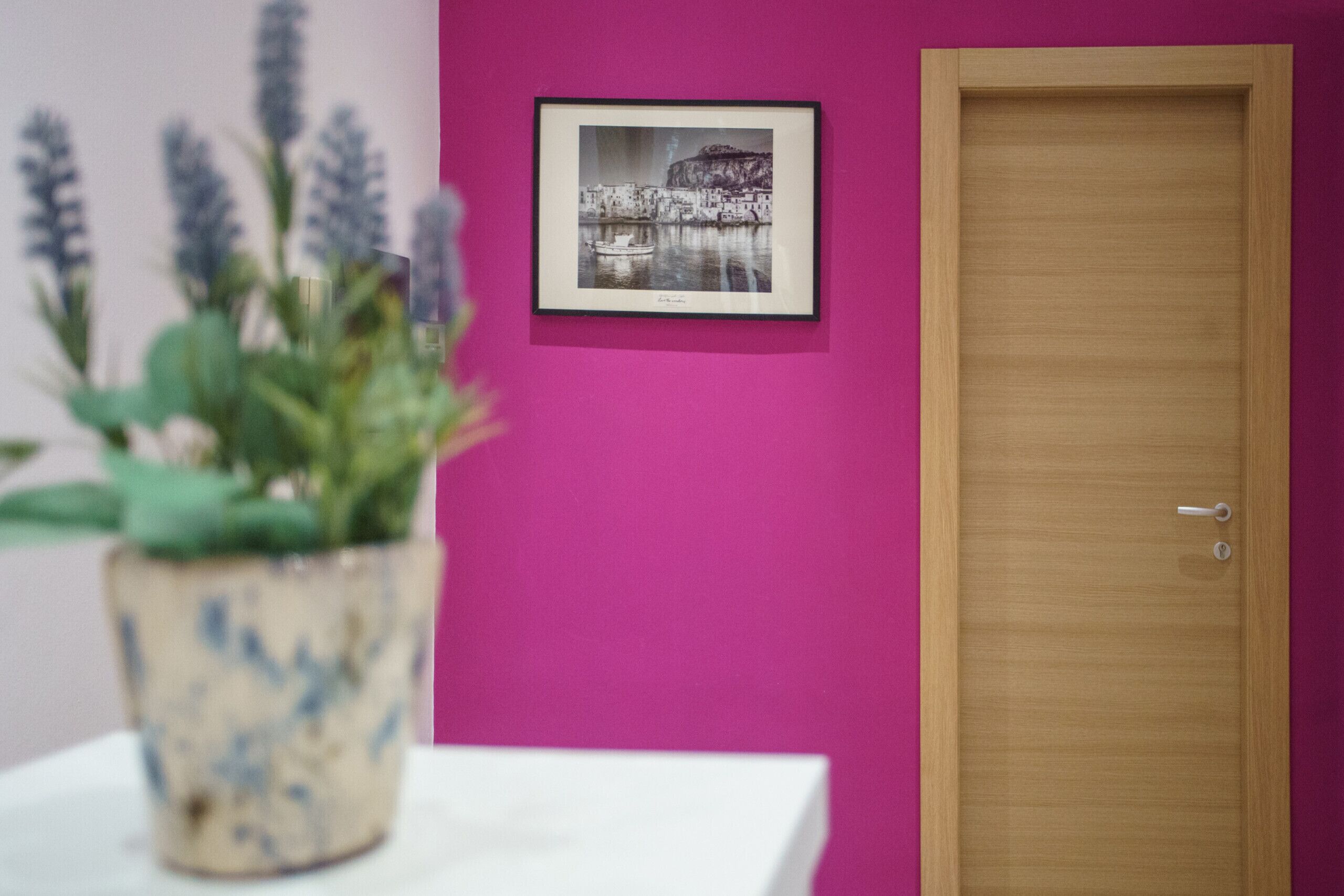 Une pièce avec une porte en bois, une photographie en noir et blanc encadrée accrochée au mur et une plante en pot posée sur une table blanche.
