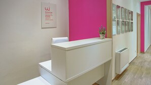 A reception desk with a white counter and a pink accent wall. - Seaview Rooms - Double Room by Wonderful Italy (Cefalù)
