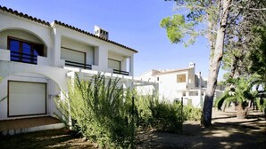 A white building with a tiled roof, a balcony, and a garage door. - Townhouses El Pinar   Rentalmar (Miami Platja)
