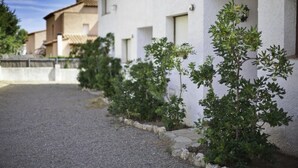 A row of white buildings with small windows and a gravel path in front. - Townhouses El Pinar   Rentalmar (Miami Platja)