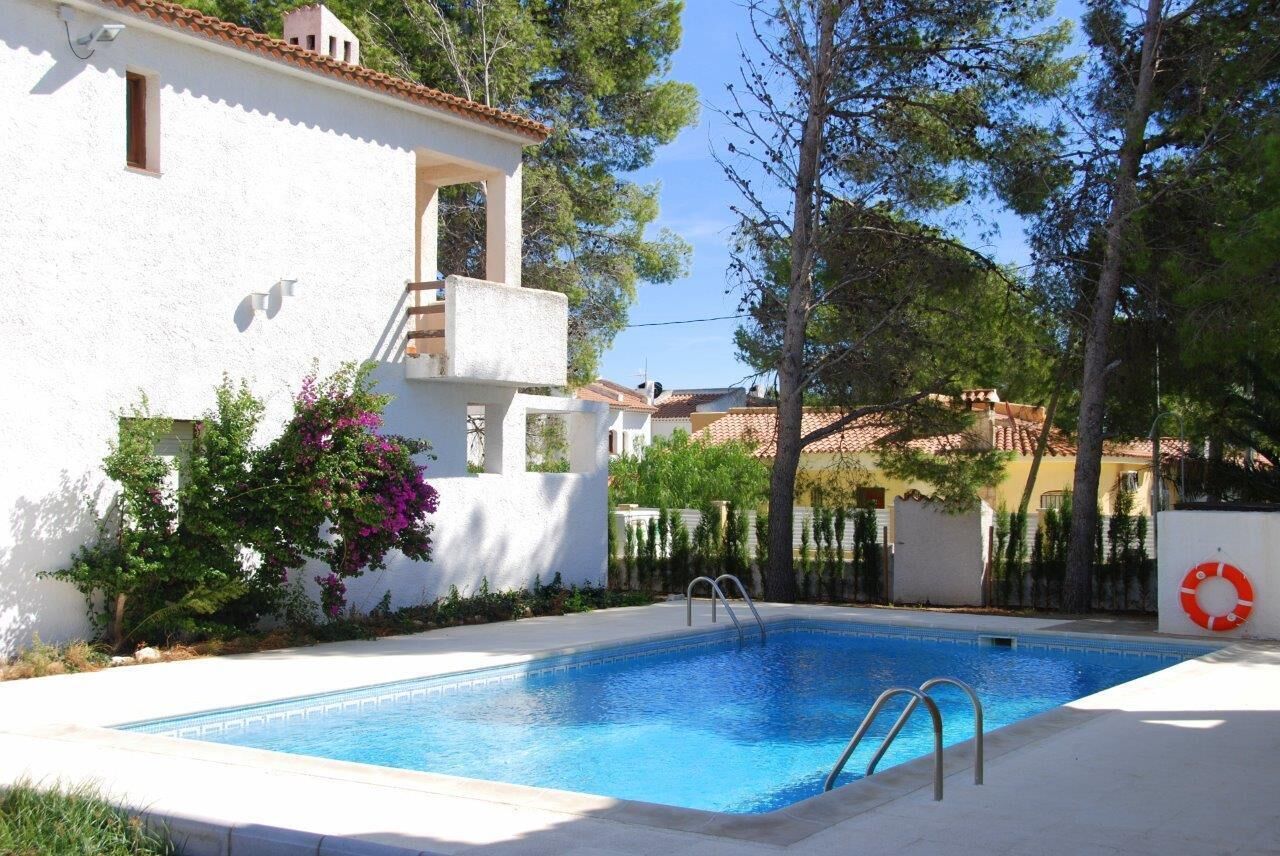 A swimming pool with a ladder, surrounded by white walls and trees.