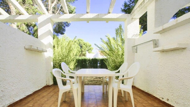 A patio with a white table and four chairs, surrounded by white walls and a wooden floor. - Townhouses El Pinar   Rentalmar (Miami Platja)