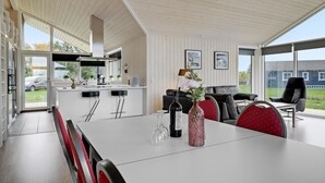 Une cuisine moderne dotée d’un grand îlot central, un coin repas avec une table blanche et un salon avec un canapé noir.