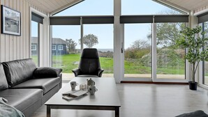 Un salon moderne avec un canapé, une table basse et un fauteuil. Une grande fenêtre offre une vue sur une maison et sur la verdure environnante.
