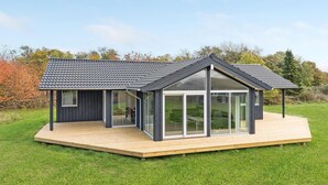 Une maison moderne avec une grande façade vitrée et une terrasse en bois.