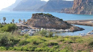 Una zona costanera amb una illa rocosa, embarcacions i un port esportiu.