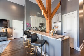 A modern kitchen with a central island, bar stools, and a built-in microwave. - 💜Beautiful City-Getaway, 2Bed/2Bath with Queen Sleeper+Balcony - The Iris (New Orleans)