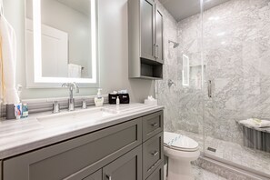 Un baño moderno con ducha de mármol, un espejo grande y un tocador con lavamanos y armarios.