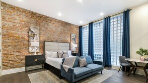 Une chambre moderne avec un mur en briques, un lit avec une tête de lit, un canapé bleu, une table à manger et une chaise.