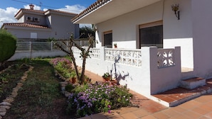 A white house with a tiled roof, a small garden with purple flowers, and a white fence. - INNOUTHOME GARDEN, SWIMING-POOL,BEACH AT 150M,BBQ, AC AND WIFI_VIRGEN CINTA II (L'Ametlla de Mar)