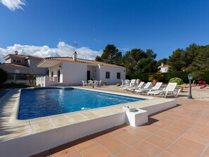 A swimming pool with white lounge chairs and a white building with a tiled roof.