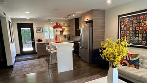 A modern kitchen with a central island, a refrigerator, and a dining area with a sofa and a coffee table. - Contemporary Flat w/Gentleman's Vineyard -1 Block to Downtown Napa! Non-Hosted (Napa)