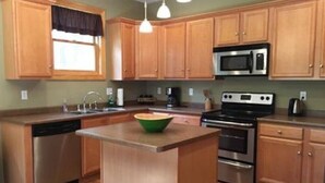Une cuisine dotée de meubles en bois, d’appareils électroménagers en acier inoxydable et de luminaires suspendus.