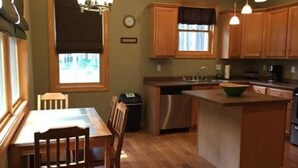 Une cuisine avec des meubles en bois, un îlot central, une table à manger avec des chaises et des luminaires suspendus.