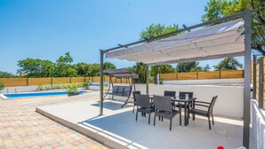 A covered outdoor seating area with a pool, chairs, and a table.