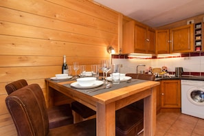 Cocina con paneles de madera, una mesa de comedor lista para cuatro comensales, lavadora y armarios de madera.
