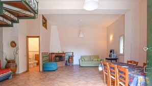 A spacious living area with a tiled floor, a sofa, a dining table with chairs, a fireplace, and a staircase with a railing. - 3 bedroom cozy home in Castellammare del G. (Castellammare del G.)