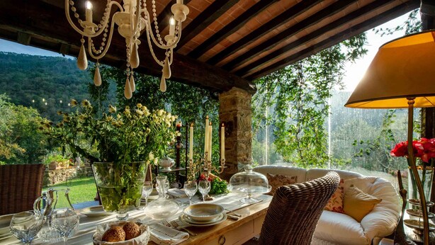 Un espace de restauration en plein air, avec une table en bois dressée pour un repas, entourée de meubles en osier et offrant une vue sur un jardin luxuriant.