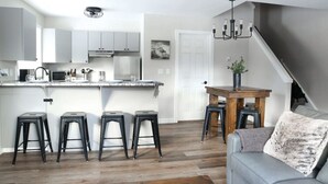 Uma cozinha moderna com armários brancos, uma ilha central com banquetas e uma mesa de jantar com cadeiras.