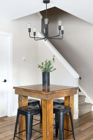 Un espace repas avec une table en bois, des tabourets noirs et un lustre noir.