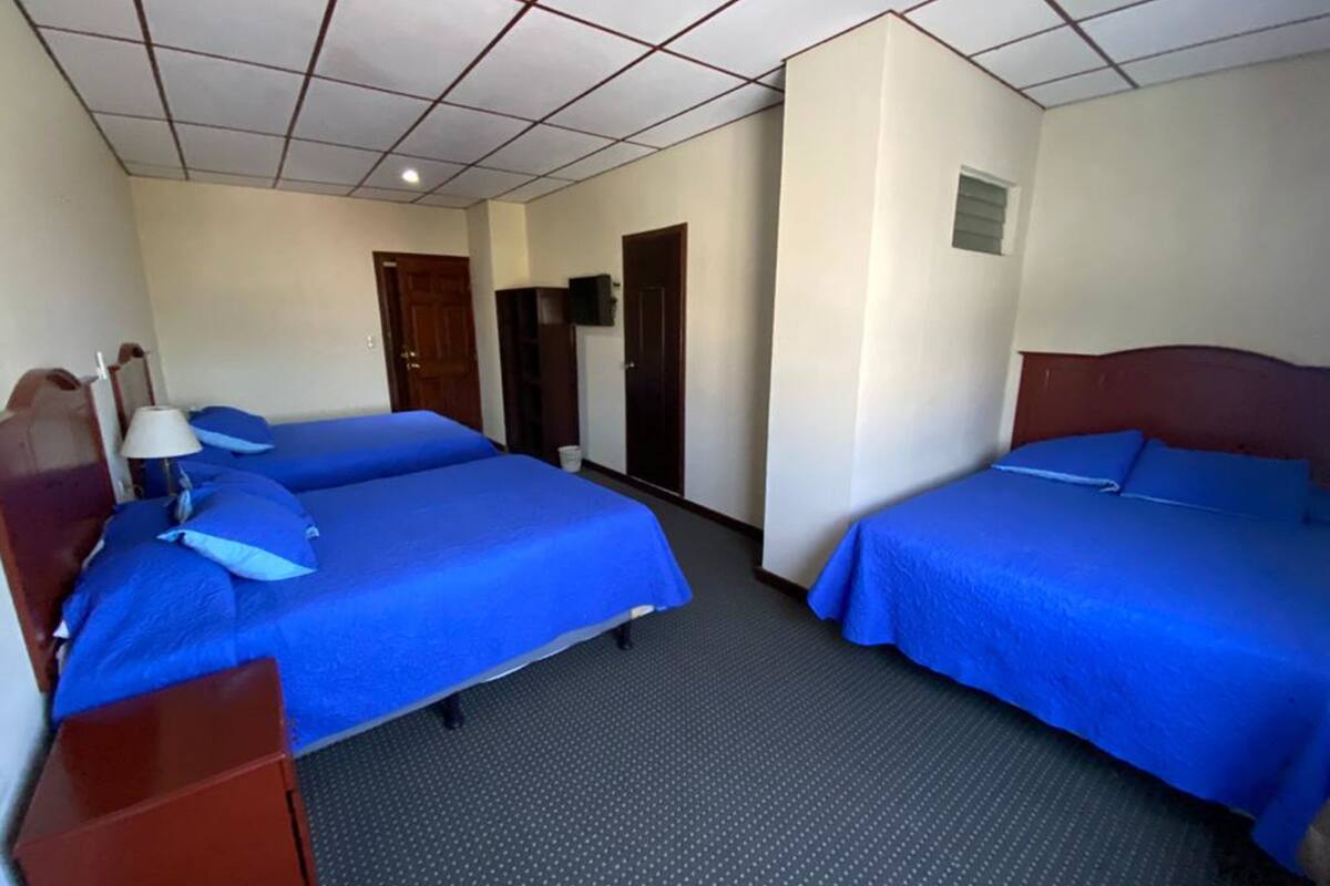 A hotel room with two beds, a desk, a lamp, and a television.