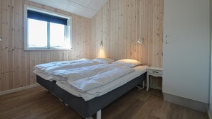 Een slaapkamer met een bed, nachtkastje, lamp en raam.