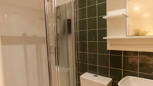 A bathroom with a glass-enclosed shower, a toilet, a sink, and a green emergency exit sign.
