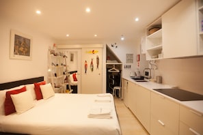 A compact hotel room with a bed, a kitchenette, and a small bathroom.