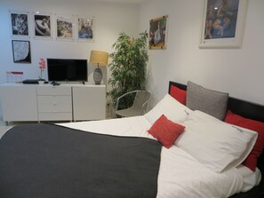 Une chambre à coucher avec un lit, un bureau avec une télévision, une chaise et une plante.