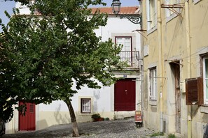 A narrow cobblestone street with buildings, a tree, and a red door. - FLH Casa Carol Mouraria (Lisbon)