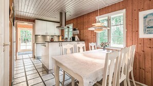 Una cocina acogedora con paredes de madera, un comedor con mantel de encaje y un ventanal con vistas a árboles.