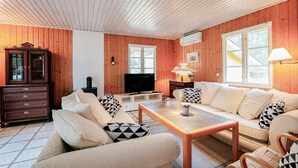 Una sala de estar acogedora con paredes de madera, un televisor, un mueble aparador y un sofá con cojines estampados.