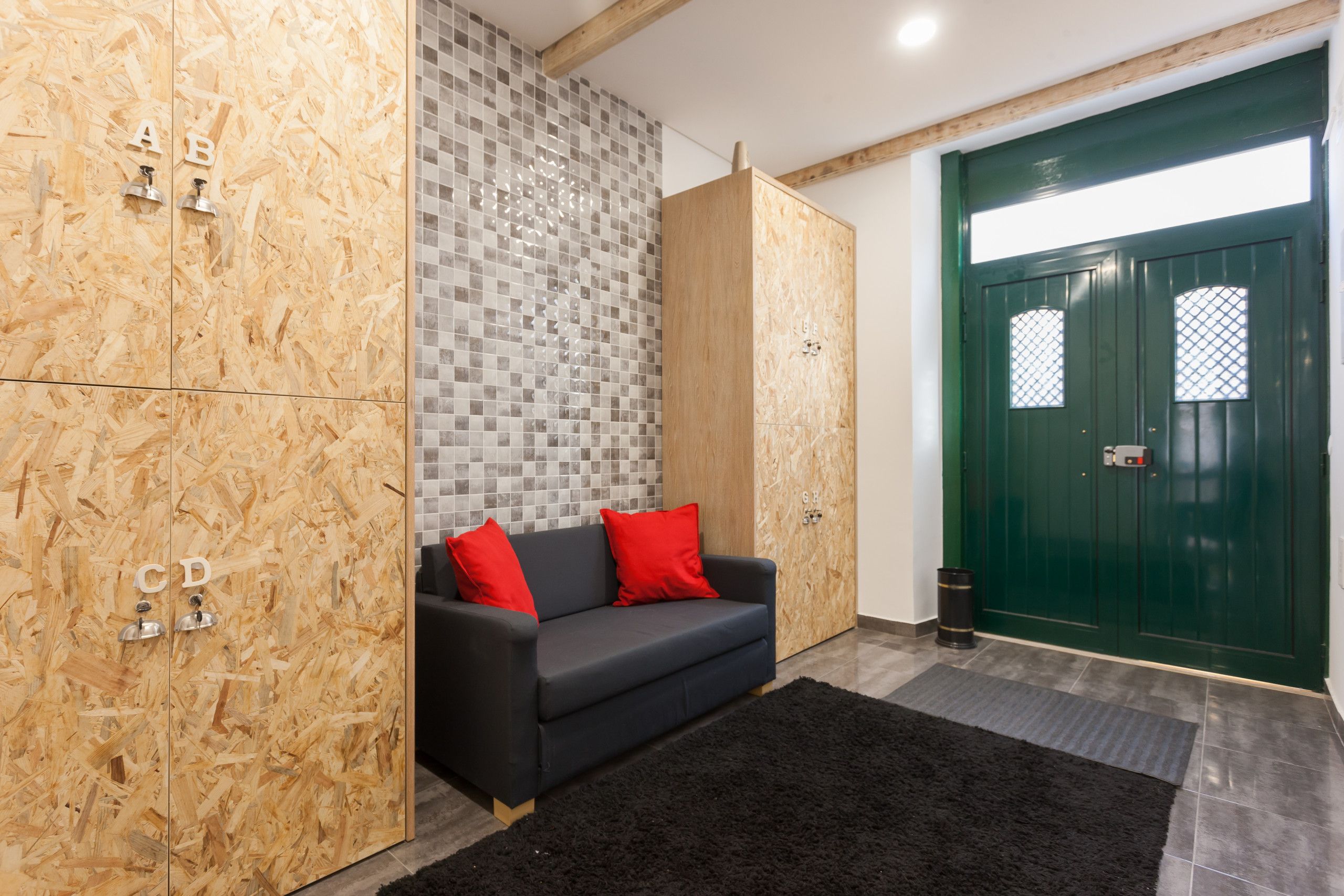A modern interior with a black sofa, red cushions, a wooden cabinet with alphabet letters, a green door, and a tiled wall.