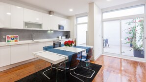 A modern kitchen with white cabinets, a dining table with blue chairs, and a black rug. - FLH Graça Artistic Studio (Lisbon)