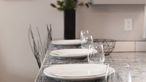 A dining table set with plates and glasses, a vase with green plants, and a wire basket on a marble countertop.