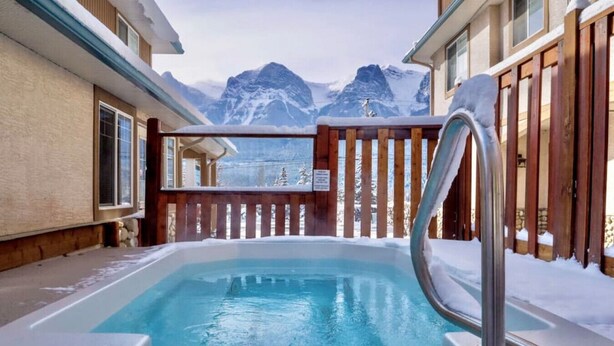 A hot tub with a wooden deck and a view of snow-covered mountains.
